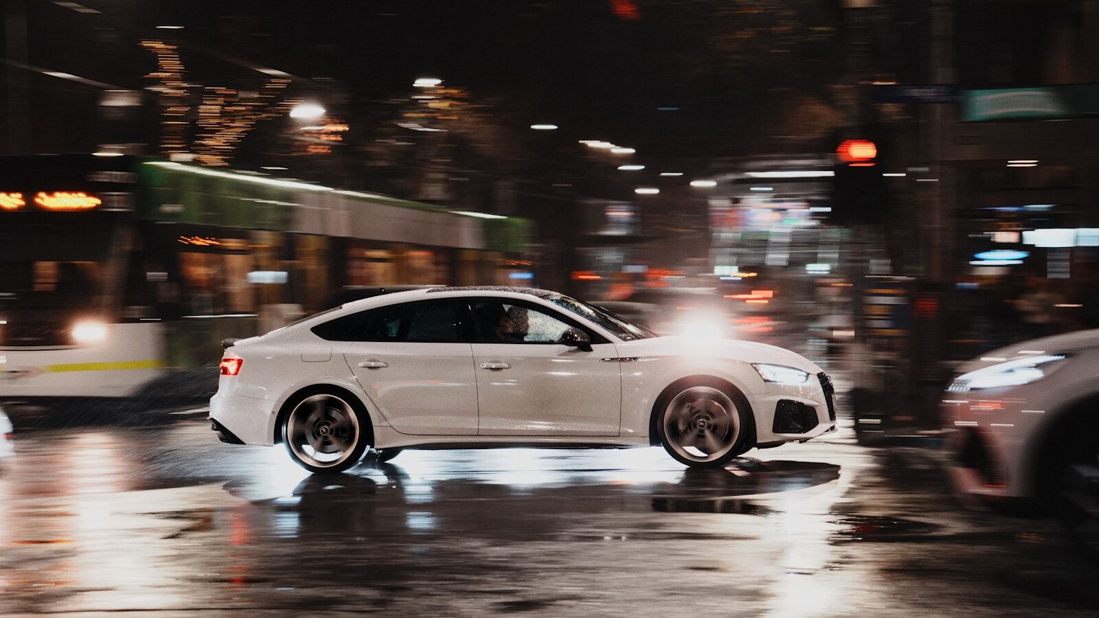 White car driving on wet city street at night